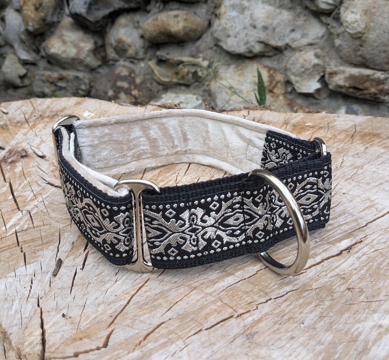 May include: A dog collar featuring a black fabric strap with a silver-toned geometric pattern, a cream-colored velvet lining, and silver-toned metal hardware including a D-ring and a sliding adjustment buckle for a secure fit around the neck.