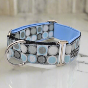 May include: A dog collar featuring a repeating geometric pattern of circles in shades of light blue, gray, white, and black. The collar includes a light blue inner lining, silver-toned metal hardware, a D-ring, and a small tag labeled Trendy Set Jerry.