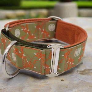 May include: A wide pet collar featuring an olive green fabric with an orange floral pattern and white circular symbols. The collar includes polished silver metal hardware, including a D-ring and a rectangular slide, with a soft orange inner lining.