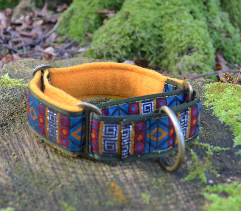 May include: A dog collar featuring a blue fabric strap with a repeating geometric pattern in red, yellow, and silver, lined with a soft mustard yellow fleece material, and equipped with antique brass-toned metal hardware including a large D-ring.