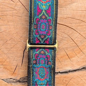 May include: A dog collar featuring a black nylon base with a woven fabric overlay in vibrant shades of hot pink, bright blue, and gold. The collar includes gold-toned metal hardware, specifically a rectangular slide adjuster and a sturdy D-ring.