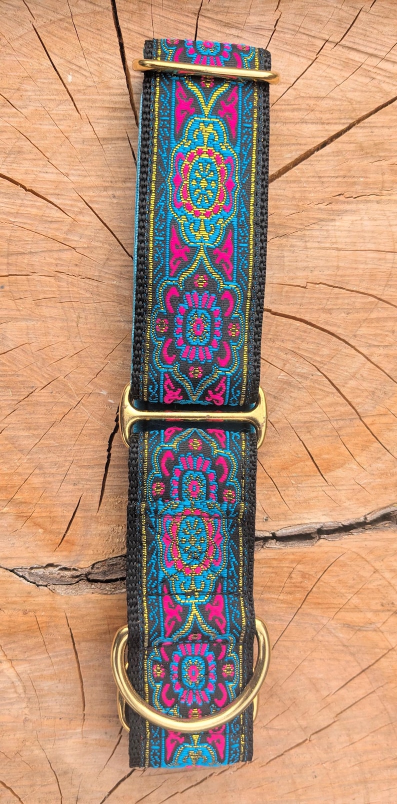 May include: A dog collar featuring a black nylon base with a woven fabric overlay in vibrant shades of hot pink, bright blue, and gold. The collar includes gold-toned metal hardware, specifically a rectangular slide adjuster and a sturdy D-ring.