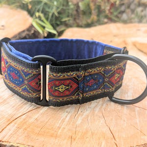 May include: A dog collar featuring a woven fabric strap with a repeating geometric pattern in red, blue, and yellow. The collar includes black metal hardware, including a D-ring and a sliding adjuster, and is lined with a solid blue fabric interior.