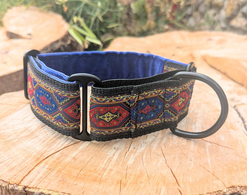 May include: A dog collar featuring a woven fabric strap with a repeating geometric pattern in red, blue, and yellow. The collar includes black metal hardware, including a D-ring and a sliding adjuster, and is lined with a solid blue fabric interior.