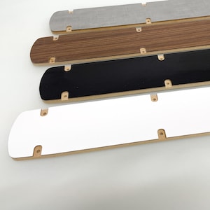 May include: Four wooden strips with different colored surfaces. The strips are stacked on top of each other. The top strip is gray, the second strip is brown, the third strip is black, and the bottom strip is white.