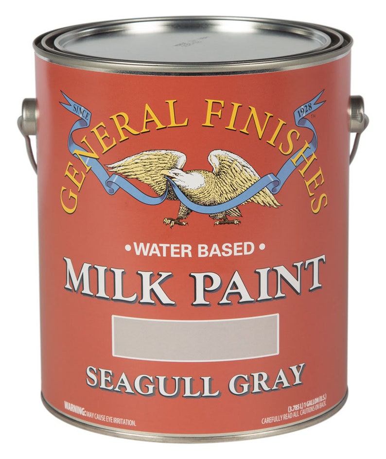 May include: A 1-gallon can of General Finishes Milk Paint in Seagull Gray. The can is red with a white eagle and blue ribbon logo. The text "WATER BASED" and "MILK PAINT" are printed in black. The can has a warning label that says "MAY CAUSE EYE IRRITATION."