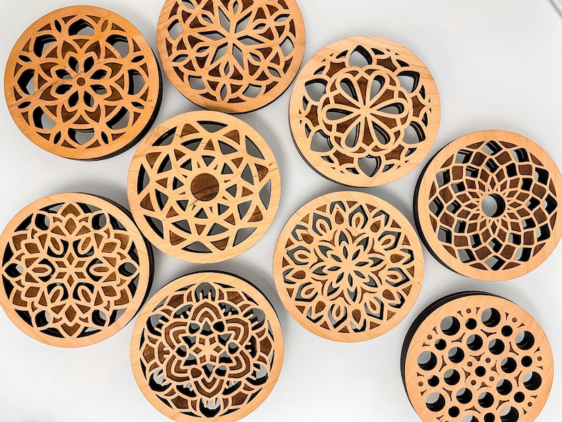 May include: Eight wooden coasters with intricate laser-cut designs. The coasters feature various geometric patterns in shades of brown.