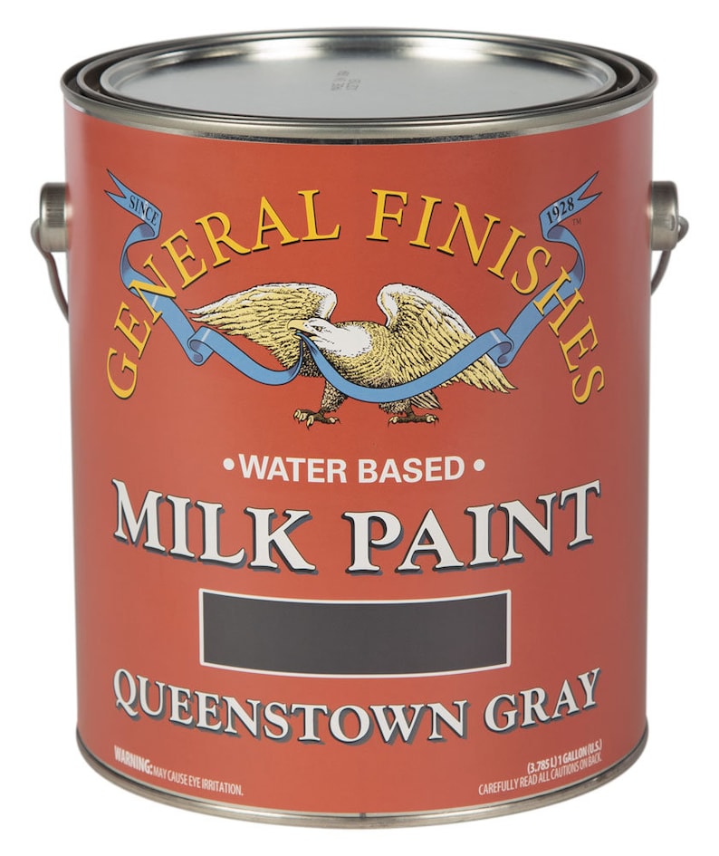 May include: A red, white, and blue can of General Finishes Milk Paint in the color Queenstown Gray. The can is labeled with the company logo and the text "Water Based" and "Milk Paint".