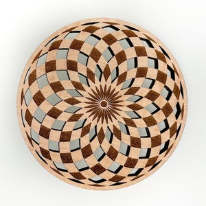 May include: A round, wooden decorative piece with a geometric pattern. The design features a series of interlocking squares and diamond shapes, creating an open, airy effect. The center has a sunburst design. The wood has a light brown color.