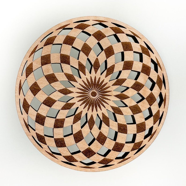 May include: A round, wooden decorative piece with a geometric pattern. The design features a series of interlocking squares and diamond shapes, creating an open, airy effect. The center has a sunburst design. The wood has a light brown color.