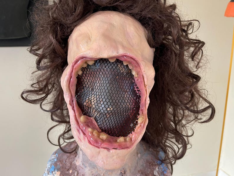 K&ouml;nnte beinhalten: Nahaufnahme einer realistischen Horror-Maske mit einem gro&szlig;en, offenen Mund und einem schwarzen Netz, das das Innere des Mundes bedeckt. Die Maske ist aus einem fleischfarbenen Material gefertigt und hat eine realistische Textur.