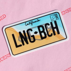 Puede incluir: Una pegatina rectangular que se asemeja a una placa de matrícula de California. La pegatina presenta el texto "LNG•BCH" en letras negras en negrita, con "California" encima. El fondo tiene una escena de playa con tonos azules y amarillos.