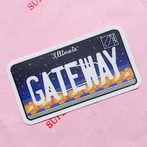Puede incluir: Una pegatina rectangular con un diseño de matrícula de Illinois. La placa dice "GATEWAY" en letras blancas sobre un fondo azul oscuro con estrellas. La parte inferior tiene un diseño de llama naranja y amarilla.