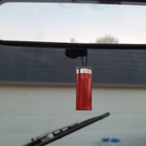 May include: A red shotgun shell hanging from the rearview mirror of a car.