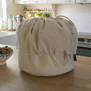 Könnte beinhalten: Eine beige Canvas-Tasche mit Kordelzug und einem kleinen schwarzen Etikett. Die Tasche liegt auf einer Holzarbeitsplatte in einer Küche.