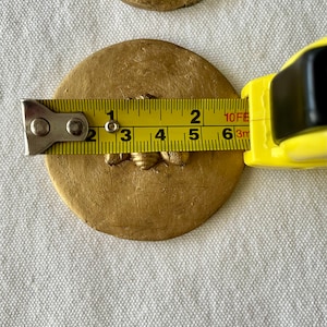May include: A gold-colored round ceramic coaster with a bee design. The coaster is 2 inches in diameter.