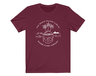 May include: A maroon t-shirt with a white graphic design of a skull with a palm tree island on top. The text around the skull reads "USS Makin Island (LHD 8) Est. 2009 Raider Flask Company".