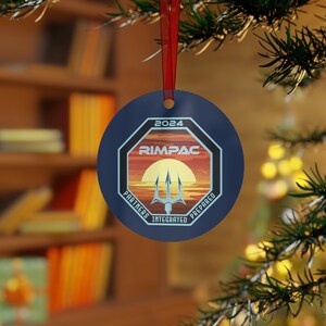 May include: A blue round Christmas ornament with a white octagon shape in the center. The octagon has a sunset scene with a trident and the text "2024 RIMPAC PARTNERS INTEGRATED PREPARED".