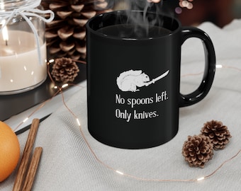 May include: Black coffee mug with a white graphic of a squirrel holding a sword. The text on the mug reads "No spoons left. Only knives."