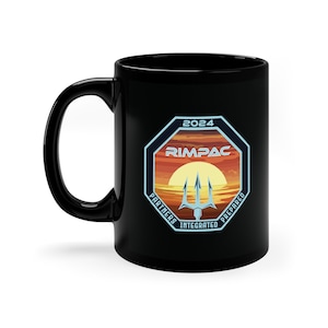 May include: Black ceramic mug featuring a colorful graphic with the text "2024 RIMPAC". The graphic includes a trident, a sunset, and the words "Partners Integrated Prepared". The mug has a large handle.