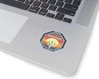 May include: A sticker with a sunset background and a trident in the center. The text "2024 RIMPAC PARTNERS INTEGRATED PREPARED" is around the trident.