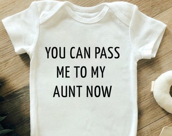 Może przedstawiać: Białe body dla dziecka z czarnym napisem "YOU CAN PASS ME TO MY AUNT NOW". Body z krótkim rękawem ma zapięcie na zatrzask. Zdjęcie zrobiono na drewnianej powierzchni.