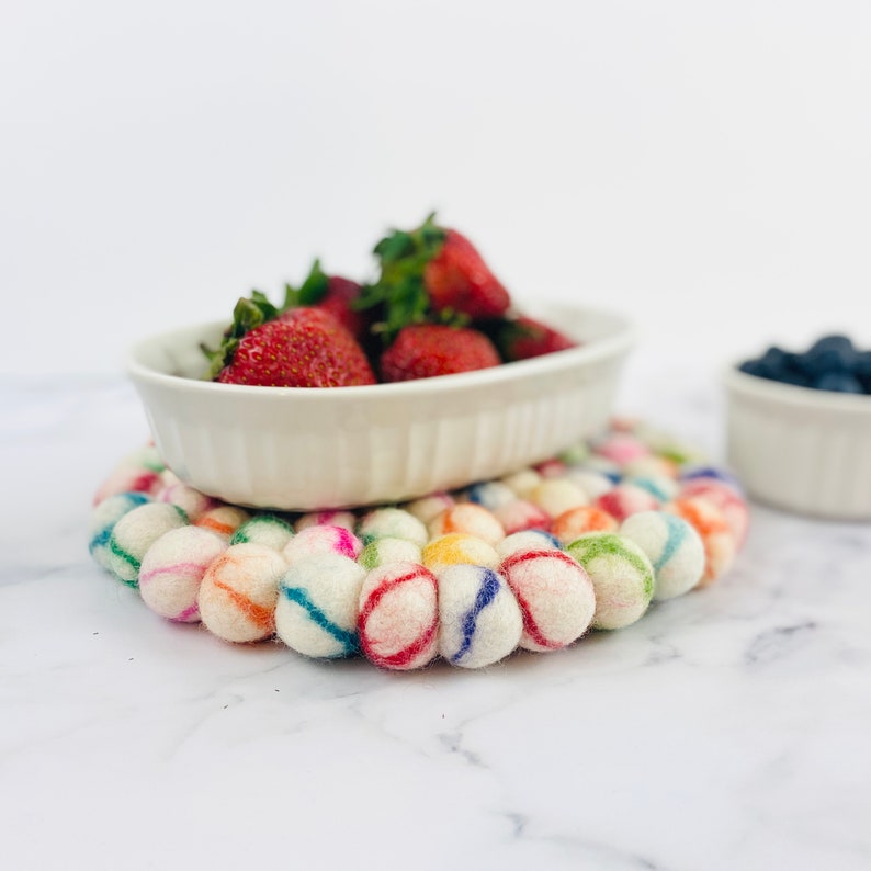 K&ouml;nnte beinhalten: Eine wei&szlig;e Keramik-Schale gef&uuml;llt mit frischen Erdbeeren steht auf einem bunten Filzuntersetzer. Der Untersetzer besteht aus runden, wei&szlig;en Filzkugeln mit bunten Streifen.