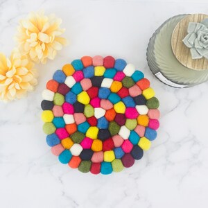 K&ouml;nnte beinhalten: Ein runder, bunter Filzuntersetzer aus vielen kleinen Filzkugeln in verschiedenen Farben, darunter Rot, Blau, Gr&uuml;n, Gelb, Orange, Rosa und Wei&szlig;.