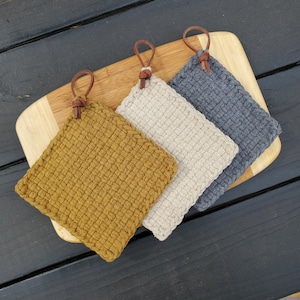 May include: Three crocheted pot holders with leather loops. The pot holders are in shades of gray, beige, and mustard yellow.