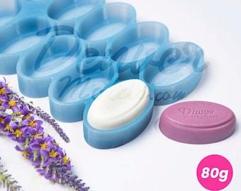 May include: A light blue silicone soap mold with oval-shaped cavities, holding a white soap bar. A purple soap bar and lavender sprigs are also present. The image includes the text "80g" and "Denver Silicone Molds."