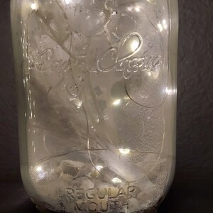 May include: A clear glass jar with a white label that reads "Regular Mouth" and a white inscription that reads "Ball." The jar is filled with white rocks and a string of white lights.