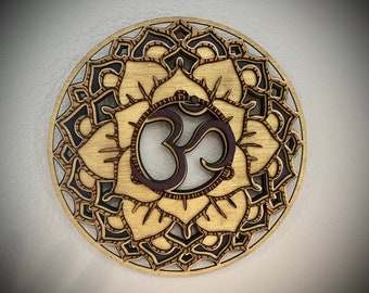 May include: A wooden mandala with a brown and black design featuring the Om symbol in the center.