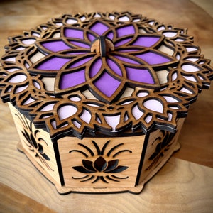 May include: A wooden box with a purple and white mandala design on the lid. The box is intricately carved with a floral pattern and has a hinged lid.