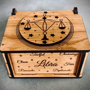 May include: A wooden box with a Libra zodiac sign on the lid. The box is decorated with stars and the words "Tacitful, Charming, Clever, Fair, Romantic, Diplomatic".