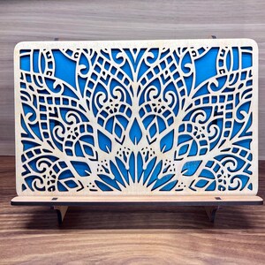May include: A wooden decorative wall art piece with a blue and white geometric design. The art is on a stand and has a cutout design.