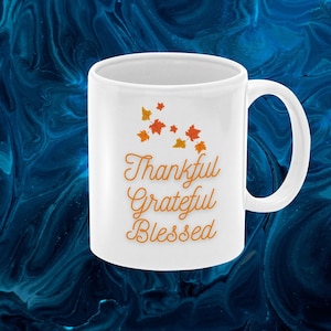 May include: White ceramic coffee mug with a design of orange and yellow fall leaves and the text "Thankful Grateful Blessed".