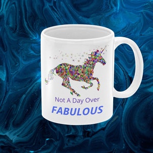 May include: White ceramic mug with a colorful mosaic unicorn design and the text "Not A Day Over FABULOUS" in blue.