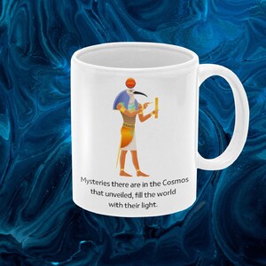 May include: White ceramic coffee mug with a colorful illustration of an Egyptian god holding a measuring tool. The text "Mysteries there are in the Cosmos that unveiled, fill the world with their light." is printed on the mug.