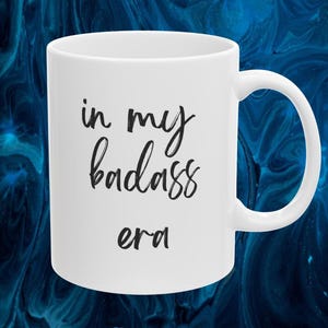May include: White ceramic mug with a curved handle. The mug features the phrase "in my badass era" in black script and sans-serif font.
