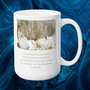May include: White ceramic mug with a winter scene featuring a woman in a white dress and a forest background. The mug has the text "I am thankful for my health. I am thankful for my family. I am thankful for my warm home. I am thankful for the abundance in my life."