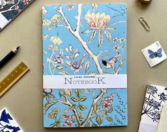 May include: A blue notebook with a floral design and a white label that reads "LAURA SOWERBY NOTEBOOK".