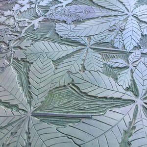 May include: A close-up of a textured surface with a repeating pattern of carved leaves. The leaves are a light green color and have a detailed vein pattern. The surface appears to be made of metal.