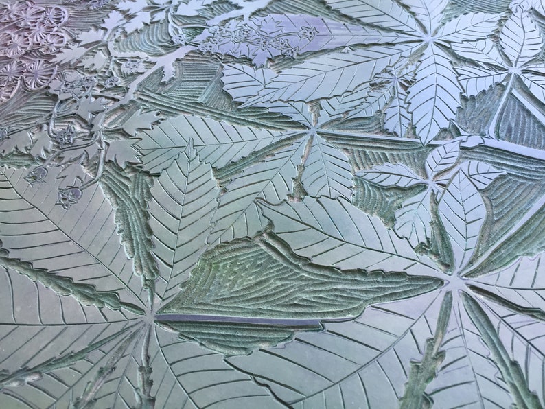 May include: A close-up of a textured surface with a repeating pattern of carved leaves. The leaves are a light green color and have a detailed vein pattern. The surface appears to be made of metal.