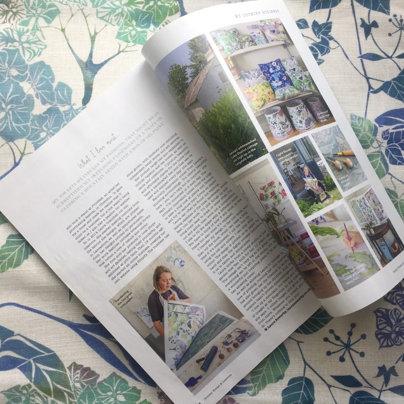 May include: A magazine spread featuring a woman painting a floral design on a large sheet of paper. The magazine article discusses the artist's love of nature and her creative process. The article also includes photos of the artist's work, including floral-themed wallpaper, cushions, and lampshades.