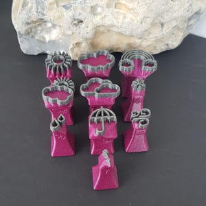 Könnte beinhalten: Eine Sammlung von pinkfarbenen, glitzernden Figuren zum Thema Wetter, darunter Sonne, Wolken, Regenbogen, Regentropfen und ein Regenschirm. Jede Figur hat eine graue Umrandung und steht auf einem Sockel.
