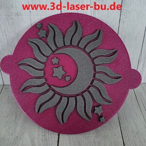 Könnte beinhalten: Eine runde, rosafarbene, glitzernde Schablone mit einem grauen Sonnen- und Monddesign. Die Sonne hat eine sichelförmige Mondform im Inneren und es gibt fünf kleine Sterne um die Sonne und den Mond.