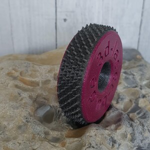Könnte beinhalten: Ein 3D-gedrucktes, kreisförmiges Objekt mit einem dunkelgrauen, strukturierten Außenrand und einem magenta-farbenen Zentrum. Das Zentrum trägt den Text "30 d-1/8". Das Objekt liegt auf einem hellen Stein.