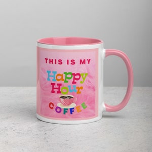 Könnte beinhalten: Eine rosa Kaffeetasse mit rosa Rand und Henkel. Die Tasse hat einen rosa Hintergrund mit einem weißen wolkenartigen Design. Der Text "This is my Happy Hour Coffee" ist in bunten Buchstaben geschrieben.