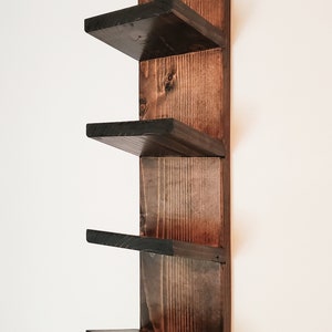 May include: A dark stained wooden wall shelf with four shelves. The shelves are square and project from a vertical backing. The wood grain is visible, and the finish is a deep brown with black edges. The shelf is designed for wall mounting.