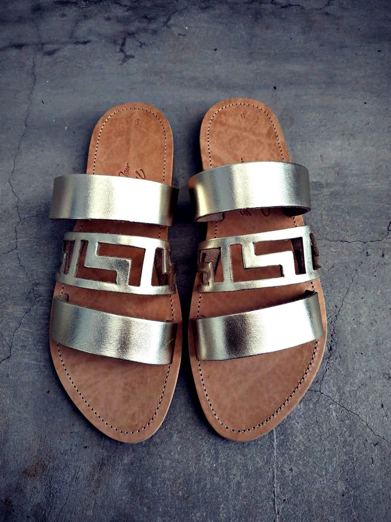 May include: A pair of gold leather sandals with three straps and a cut-out design. The sandals have a brown leather sole.